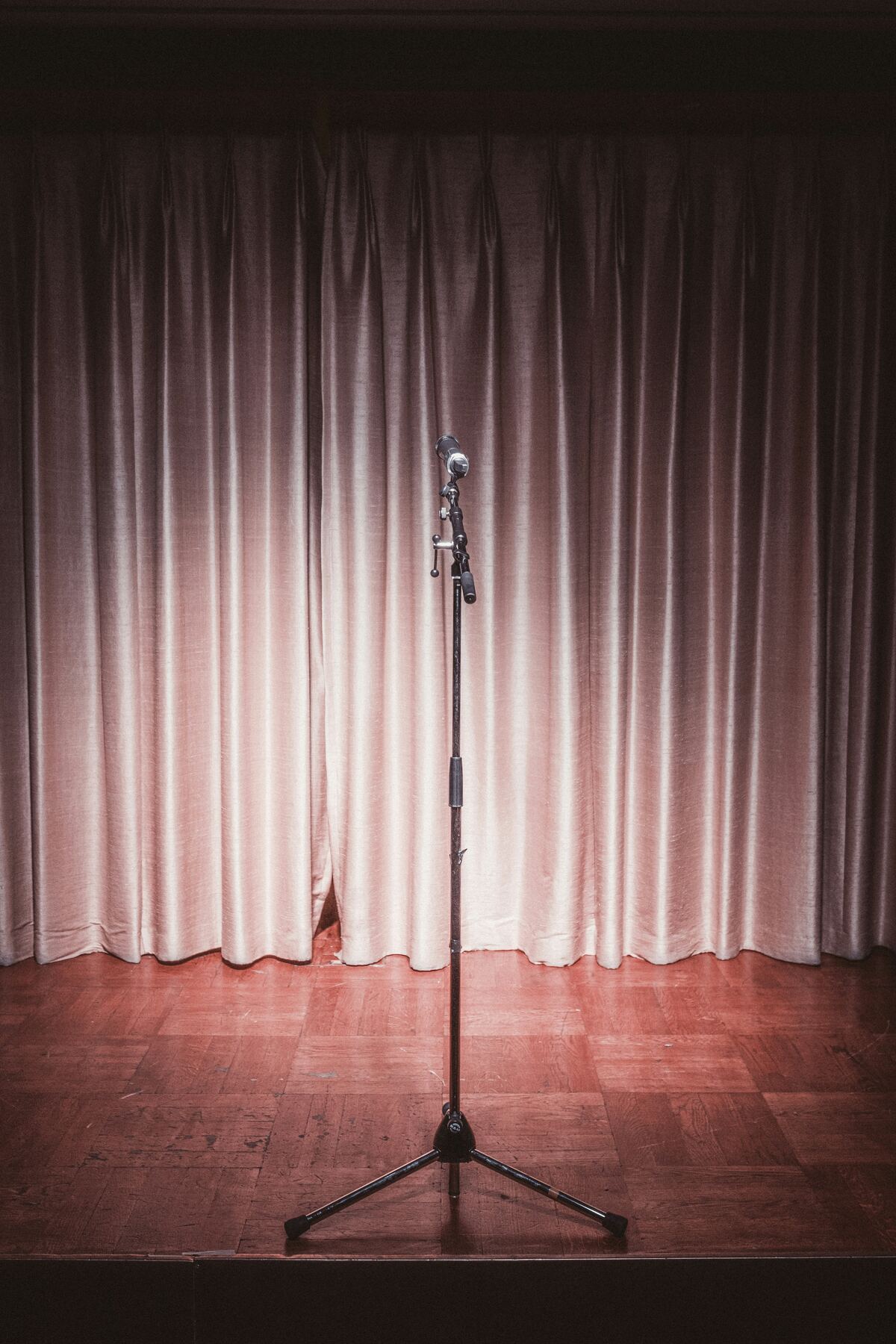 Micrófono solo en el escenario, iluminado frente al telón, esperando al próximo comediante