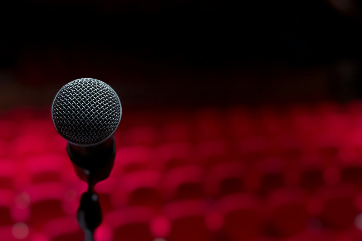 Micrófono en el escenario frente a una sala de butacas rojas todavía vacía