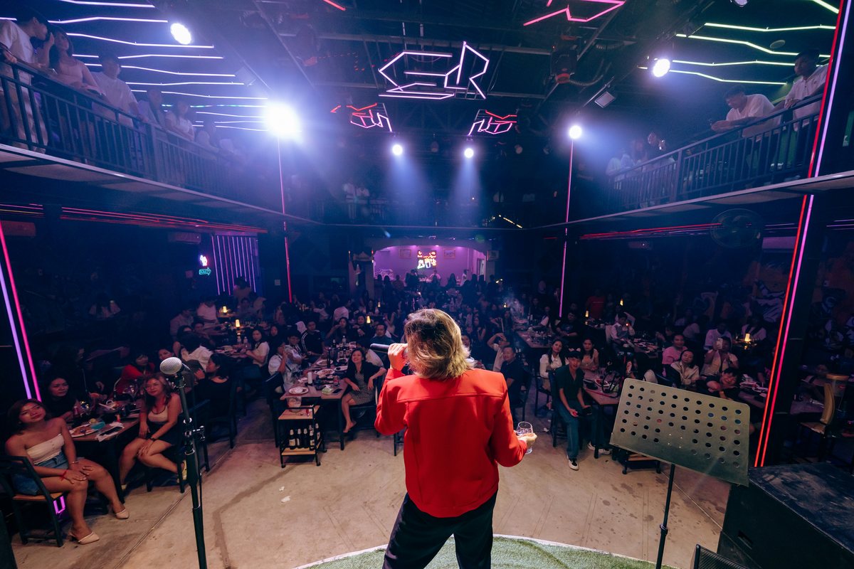 Comediante de espaldas sobre el escenario, frente a una sala llena de público